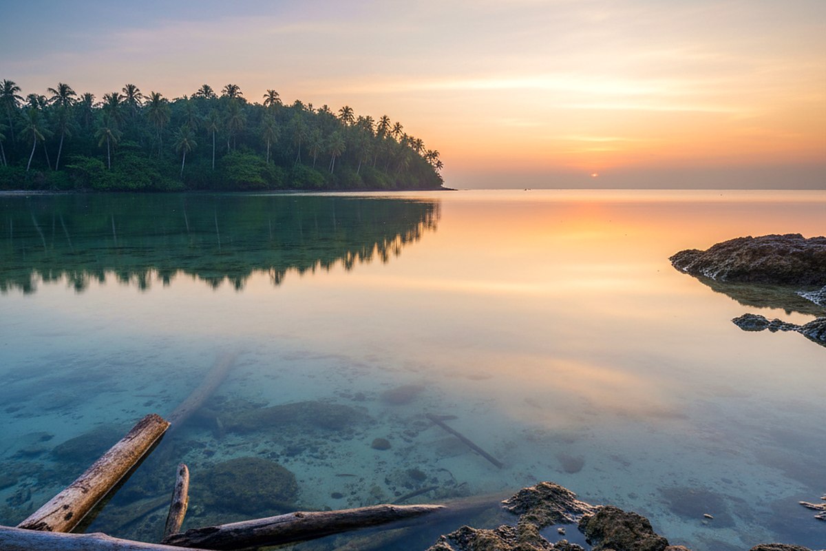 Flat calm shallow water at dawn holding a clean reflection of a headland